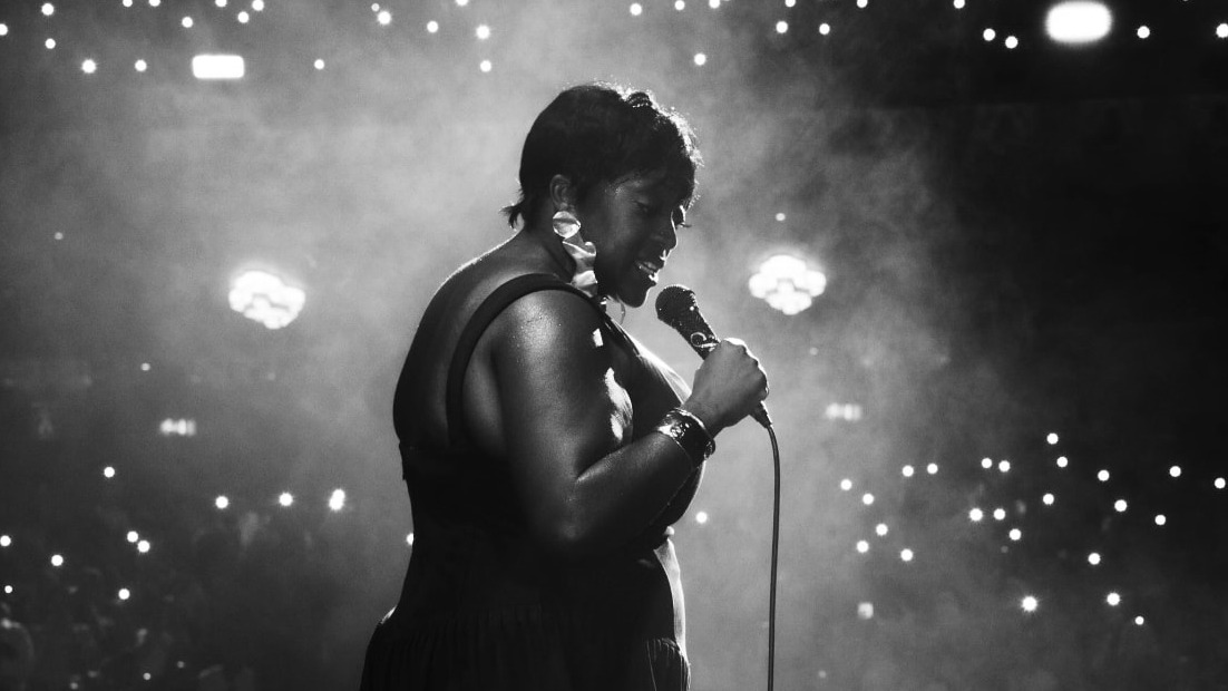 Judi Love on stage with a microphone in front of a packed theatre